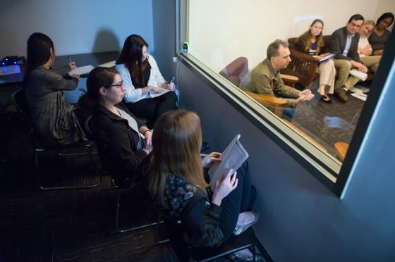 Photo of Chatham University psychology students sitting behind a mirrored window observing a therapy session. 