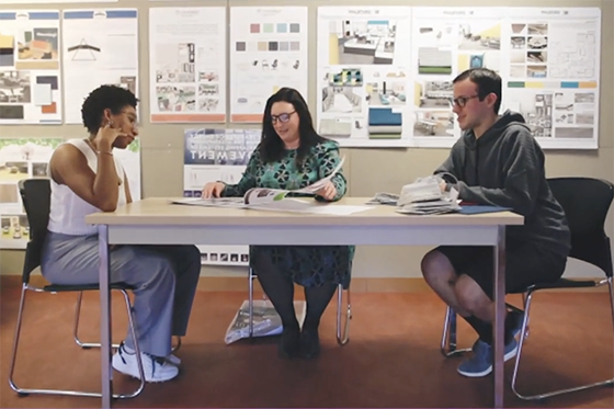 A professor and two students are seated at a table, discussing projects