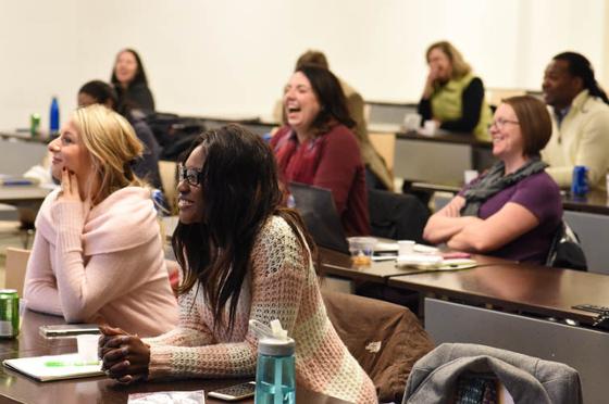 Photo of a group of Chatham University students seated in a lecture hall, smiling and interacting with an instructor out of frame.