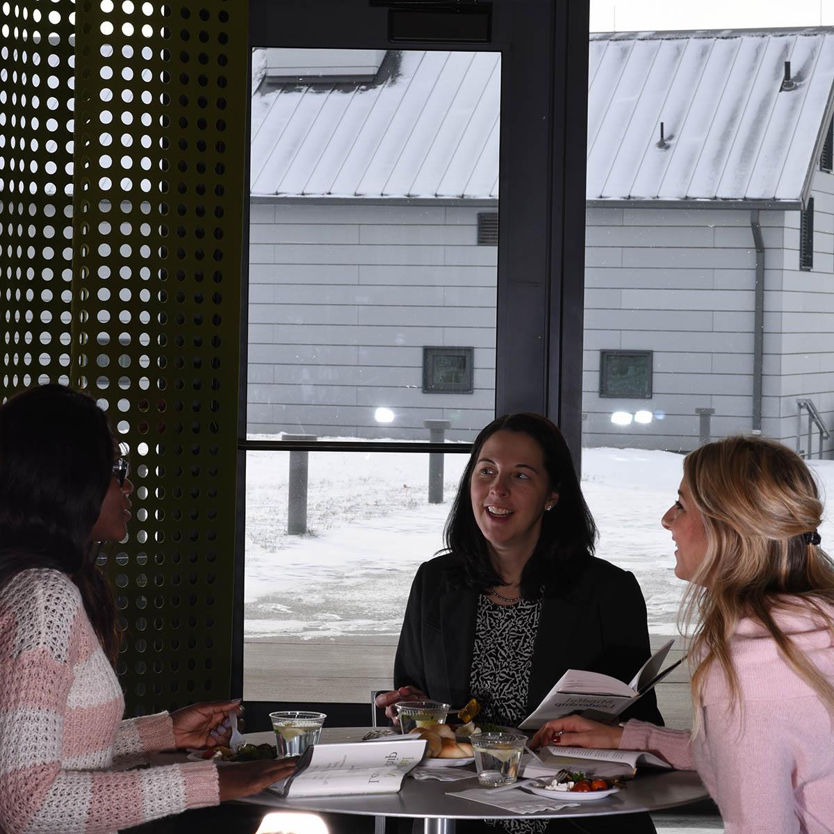 Photo of a group of women seated a table on Eden Hall Campus, laughing and speaking together