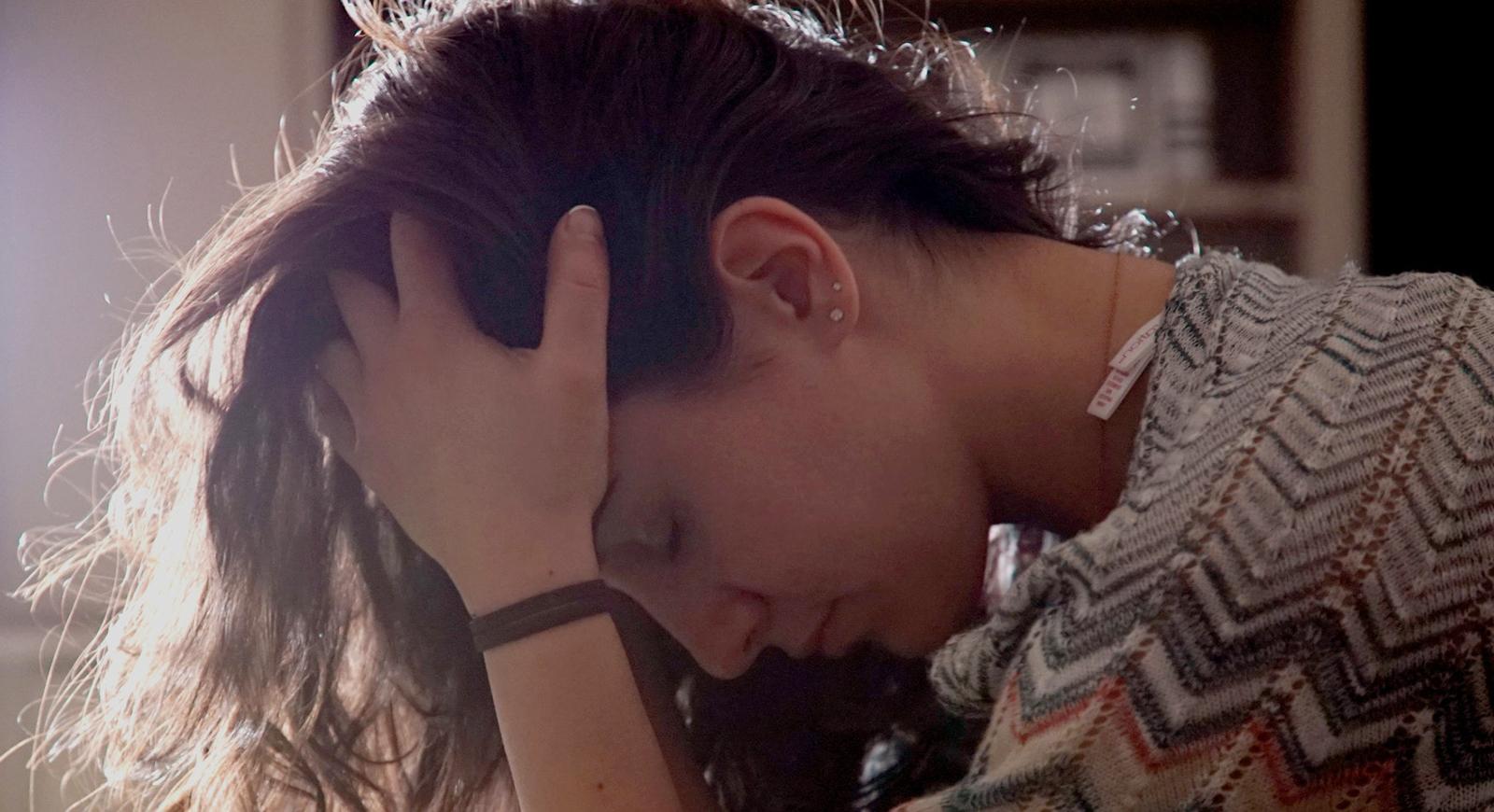 Photo of a woman leaning over with her head in hands and eyes closed.