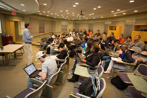 Photo of students in a lecture hall, with a professor at the front of the class