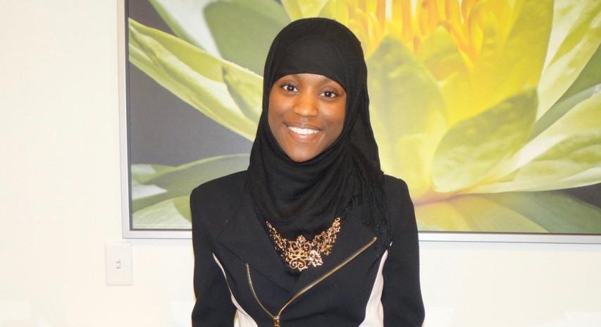 Photo of a Chatham University student wearing a hijab, smiling in front of artwork. 