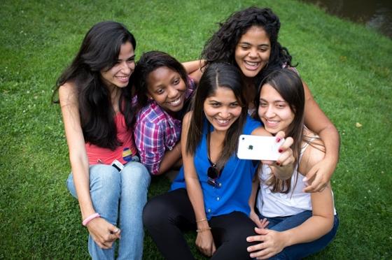 Photo of a group of five young women taking a selfie while seated outside in the grass