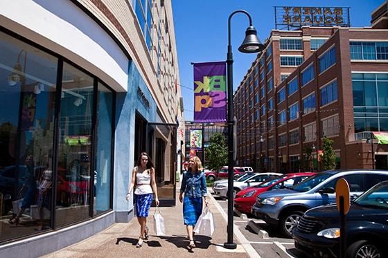 Photo of two women walking down a sidewalk in Bakery Square, Pittsburgh holding shopping bags and passing storefronts. 