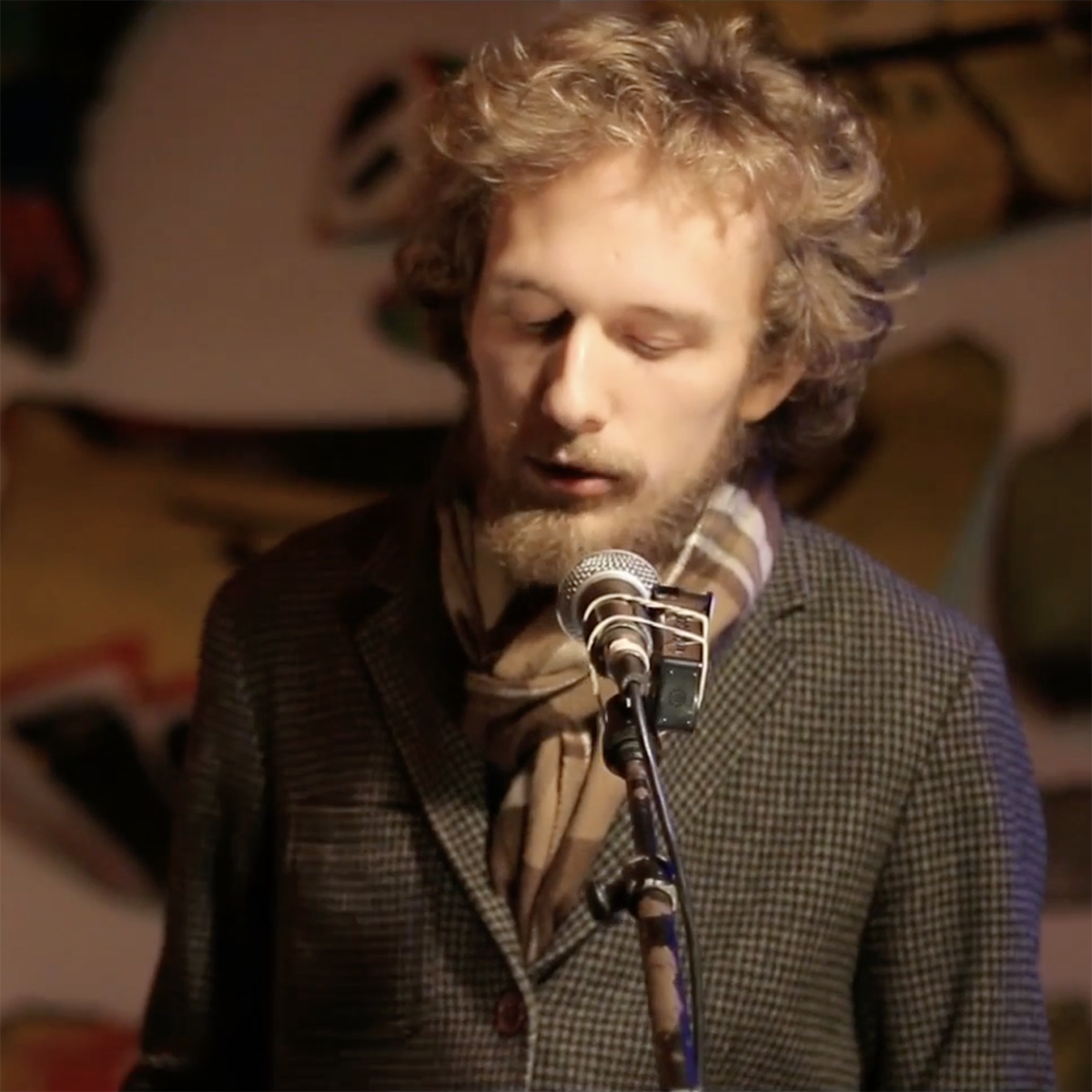 Photo of a young white man with a beard, eyes closed, speaking into a microphone